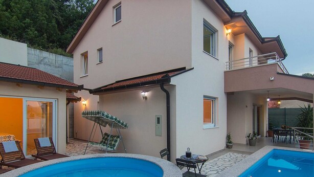 Una casa de dos pisos con piscina, mobiliario exterior y balcón.