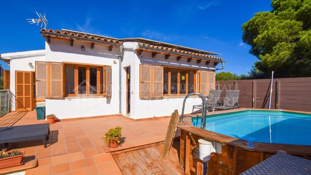 Un bâtiment blanc avec des volets en bois, une piscine et une terrasse aménagée avec du mobilier d’extérieur.