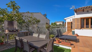 Une terrasse avec un barbecue, une table et des chaises, entourée de plantes en pot et d’une clôture.