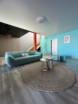 Ein modernes Wohnzimmer mit einem türkisfarbenen Sofa, einem runden Couchtisch und einem gemusterten Teppich.