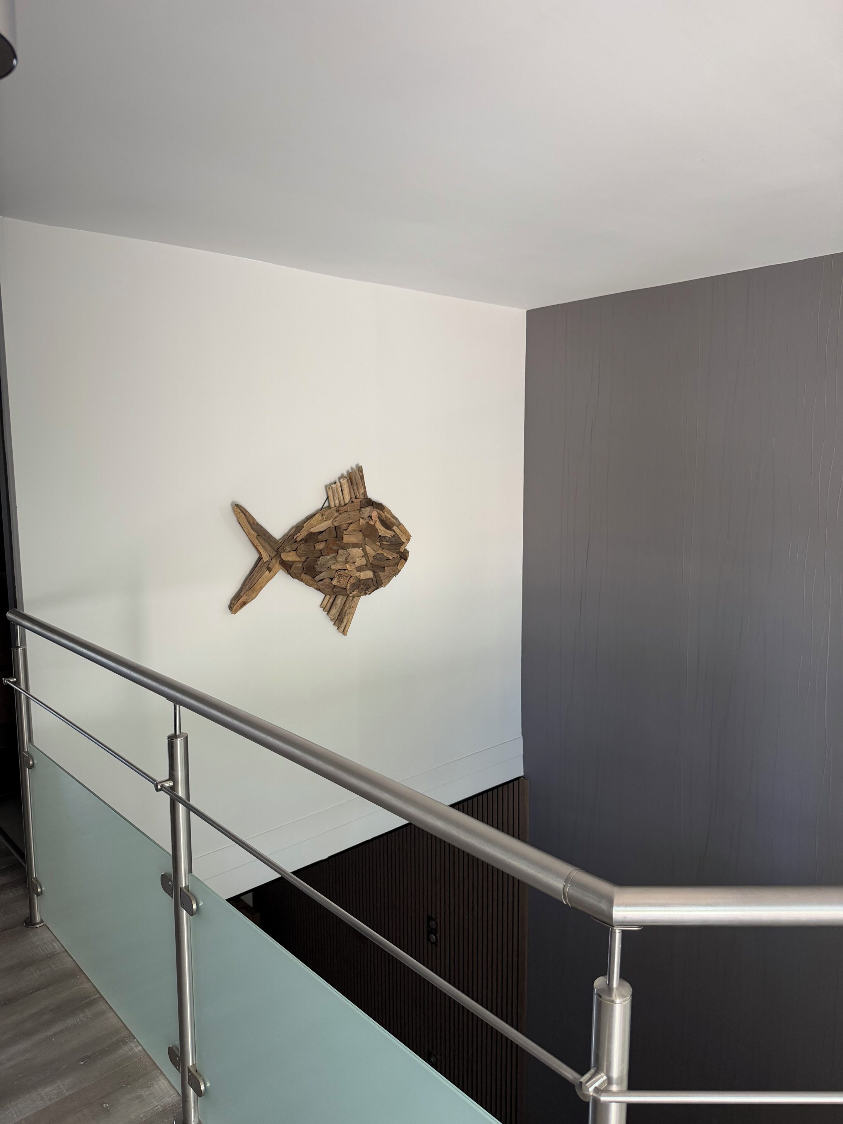 A modern interior with a staircase, a wooden wall art piece, and a glass railing.