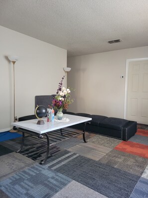 Ein Zimmer mit einem weißen Tisch, einer schwarzen Couch, einem Globus, einer Vase mit Blumen und einer Lampe.