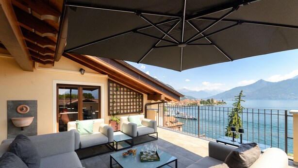 Ein Balkon mit Blick auf das Meer, eine Couch, ein Couchtisch und ein großer Sonnenschirm.