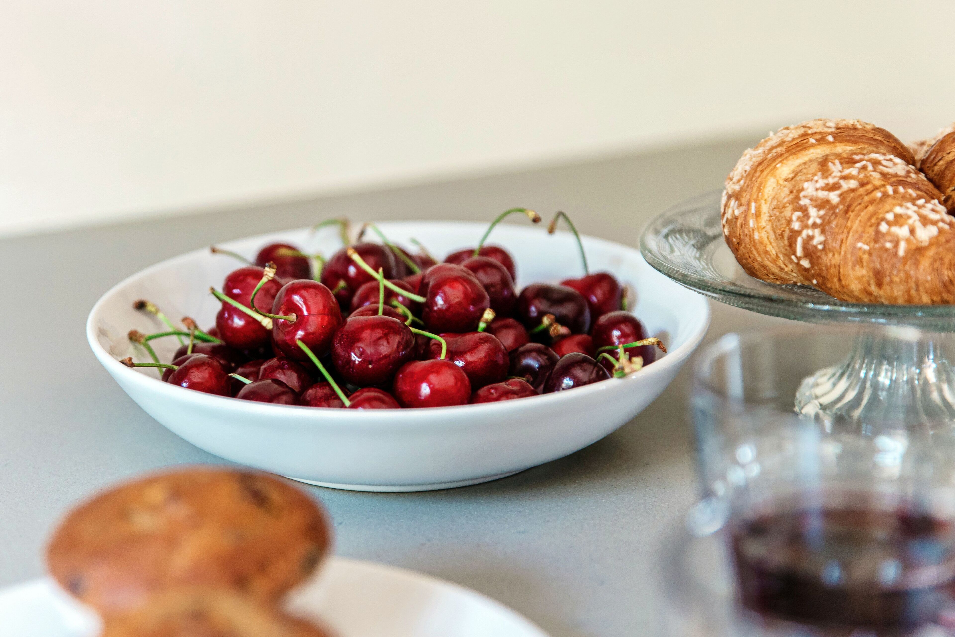 Un bol de cerezas y un croissant sobre una mesa.