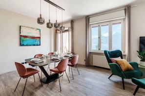 Un comedor con una mesa lista para cuatro personas, sillas, un cuadro en la pared y una ventana con vistas.