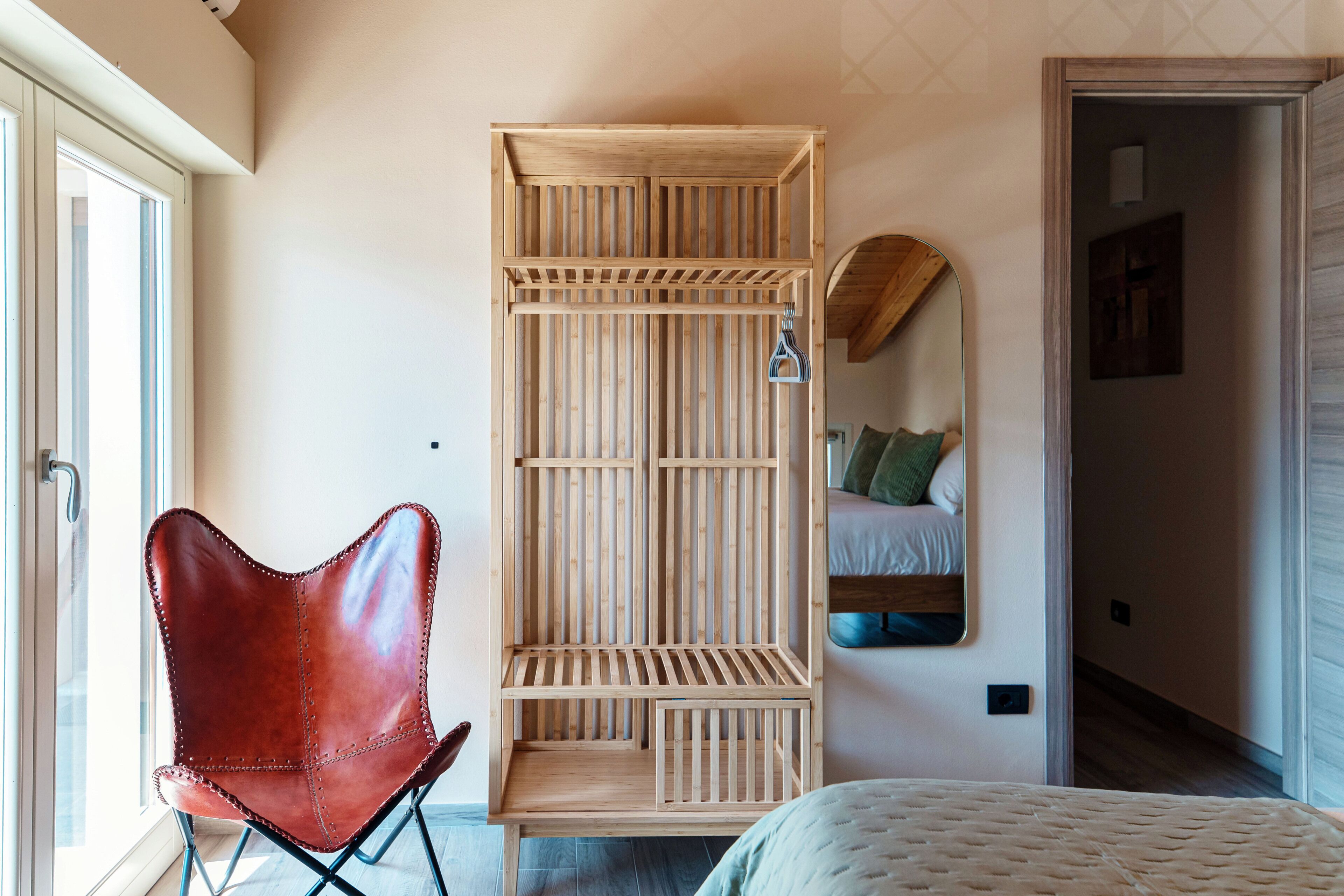 Una habitación con un armario de madera, un sillón de cuero rojo, una cama y un espejo en la pared.