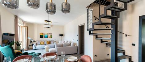 A modern dining area with a table set for four, a staircase, and a living room in the background.