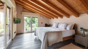 Ein Schlafzimmer mit Holzboden, einem Bett mit weißer Bettwäsche, einem Nachttisch mit Lampe und einer Schiebetür zu einem Außenbereich.