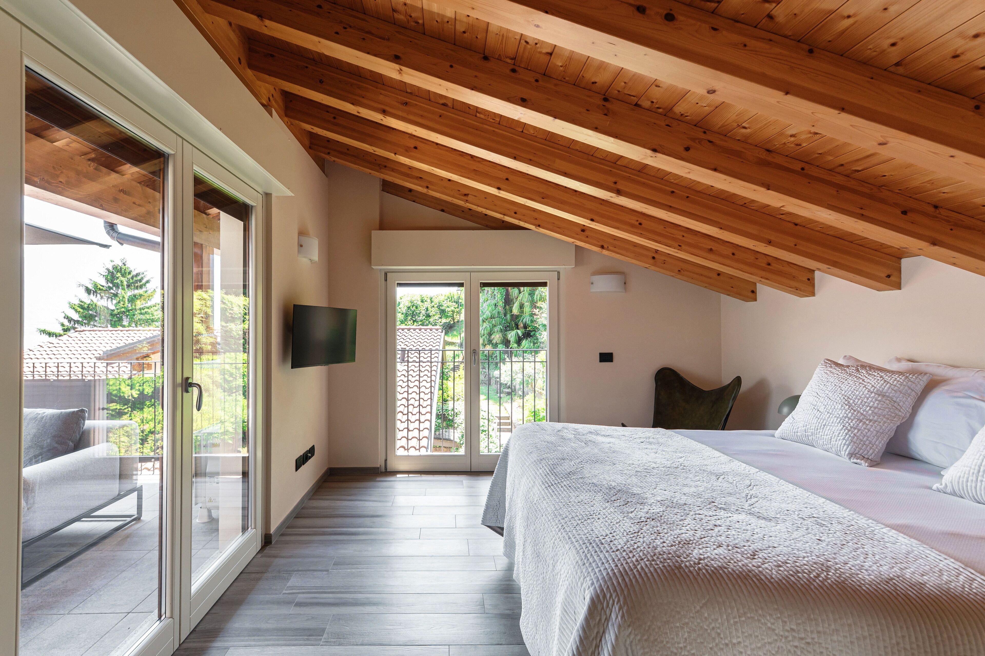Una camera da letto con soffitto in legno, un letto con biancheria bianca e una porta scorrevole in vetro che dà su uno spazio esterno.