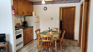 Eine Küche mit Holzausstattung, einem Kühlschrank, einem Herd, einer Kaffeemaschine und einem Esstisch mit Stühlen.