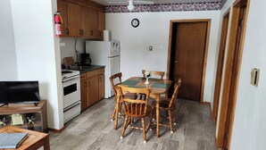 Eine kompakte Küche mit Holzausstattung, einem Herd, einem Kühlschrank und einem Esstisch mit Stühlen.