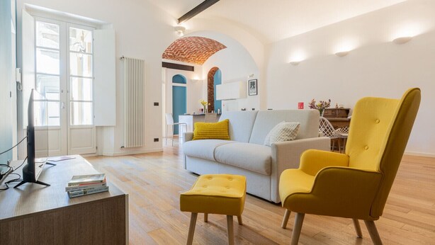 Uma sala de estar moderna com um sofá, uma poltrona amarela e uma televisão sobre uma mesa de madeira.