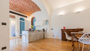 Uma cozinha moderna com arco de tijolos, banquetas de bar brancas, uma mesa de jantar de madeira e um armário branco.