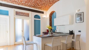 Cozinha com ilha central, banquetas brancas, máquina de café e um vaso com flores.
