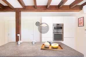 A kitchen with a granite countertop, wooden beams, white cabinets, a clock, and a framed picture. - Villa Igelak - Hossegor - Center - Lake - Pool (Soorts-Hossegor)