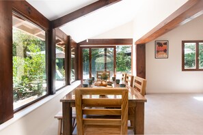 A dining area with a wooden table and chairs, large windows, and a framed picture on the wall. - Villa Igelak - Hossegor - Center - Lake - Pool (Soorts-Hossegor)