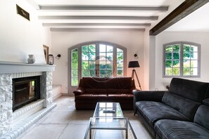 Ein Wohnzimmer mit Kamin, einem braunen Ledersofa, einem schwarzen Sofa und einem Glastisch.