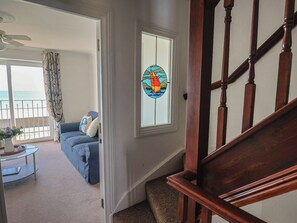 A staircase with wooden balusters, a blue sofa with cushions, a small round table with a vase, and a stained glass window depicting a sailboat. - 2 Lyme Mews (Seaton)