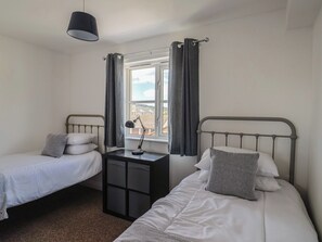 Ein Doppelzimmer mit zwei Einzelbetten, einem kleinen Tisch, einer Lampe und einem Fenster mit Vorhängen.