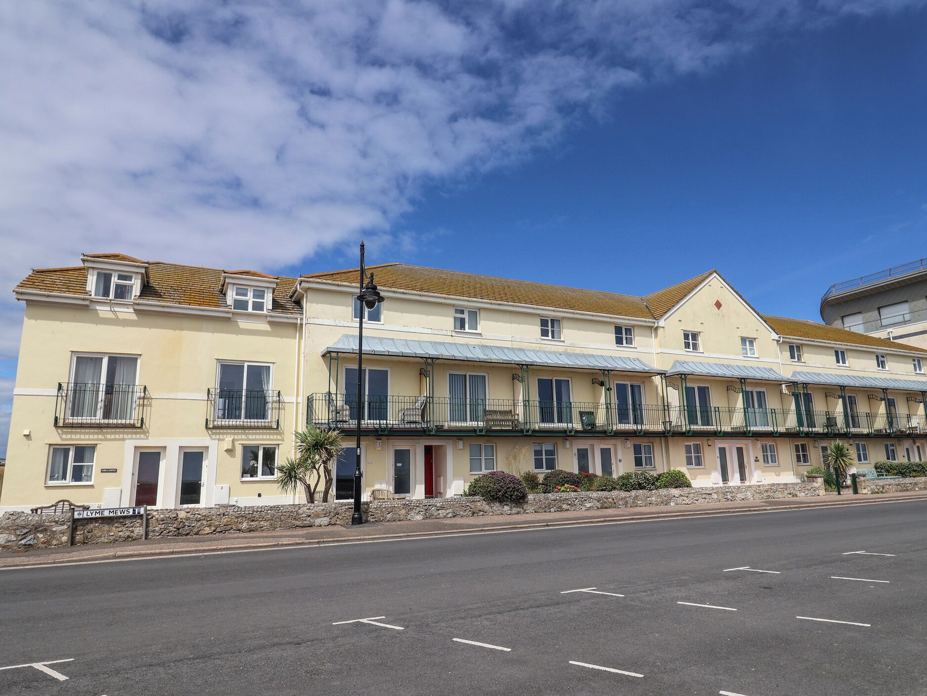 A row of two-story buildings with balconies, a clear sky, and a street in front.