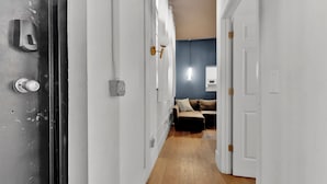 A hallway with a door on the left, a light switch, and a wall socket. - Apartmint at Arch St Philadelphia (Philadelphia)