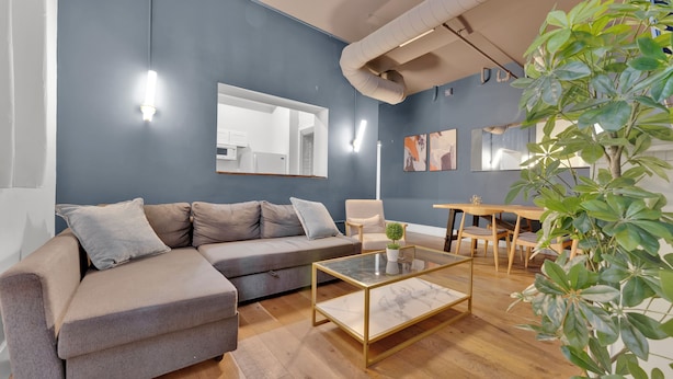 A modern living room with a sectional sofa, a glass coffee table, a dining table with chairs, and a large mirror on the wall. - Apartmint at Arch St Philadelphia (Philadelphia)