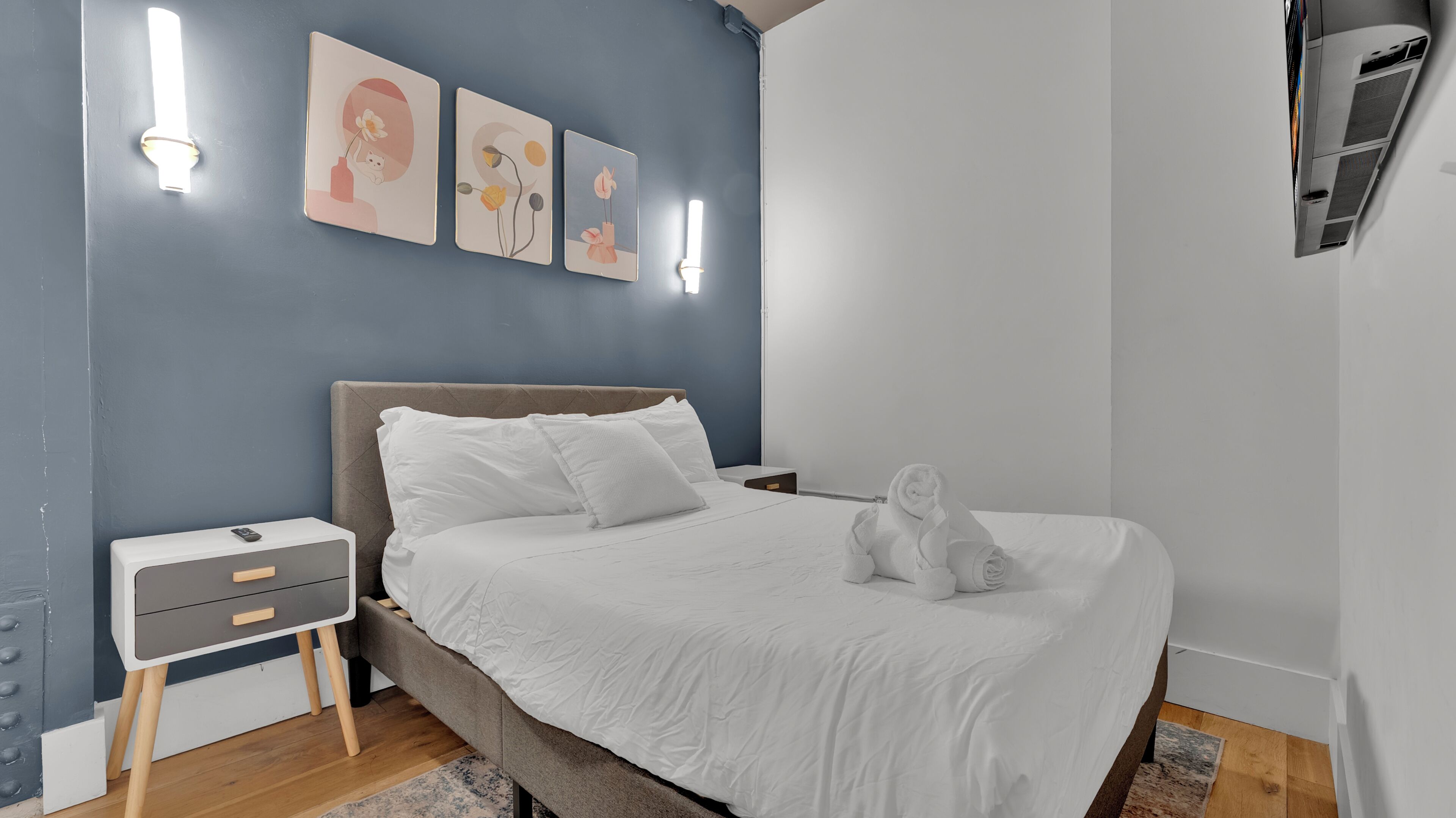 Une chambre à coucher comprenant un lit, des tables de chevet, des œuvres d’art murales et un appareil de climatisation.