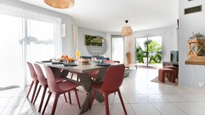 A modern dining area with a large table, red chairs, and a hanging light fixture. - Villa Alaïa - Hossegor - Cycle path - Shops (Soorts-Hossegor)