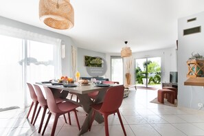 A modern dining area with a large table, red chairs, and a hanging light fixture. - Villa Alaïa - Hossegor - Cycle path - Shops (Soorts-Hossegor)