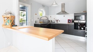 A modern kitchen with a wooden island, black cabinets, a stainless steel range hood, and a microwave. - Villa Alaïa - Hossegor - Cycle path - Shops (Soorts-Hossegor)