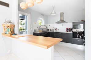 A modern kitchen with a wooden island, black cabinets, a stainless steel range hood, and a microwave. - Villa Alaïa - Hossegor - Cycle path - Shops (Soorts-Hossegor)