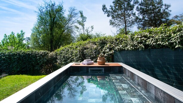 A rectangular swimming pool with a tiled edge, surrounded by lush greenery and trees. - Villa Alaïa - Hossegor - Cycle path - Shops (Soorts-Hossegor)