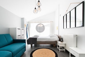 A modern bedroom with a bed, a sofa, a bedside table, a radiator, and a wall-mounted TV. - Villa Alaïa - Hossegor - Cycle path - Shops (Soorts-Hossegor)