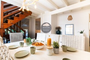 A dining area with a wooden staircase, a sign reading 'HOSSEGOR PROPERTIES,' and a table set with plates, cups, and a bowl of croissants. - Villa Patio - Seignosse - Forest - Beach - Quiet (Seignosse)