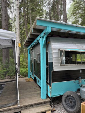 Siirrettävä koti, jonka ulkoseinät ovat turkoosin väriset, siinä on katettu kuisti ja puinen terassi.