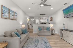 Ein modernes Wohnzimmer mit einer Couch, einem Couchtisch, einem Teppich, einem Fernseher und einer Küche im Hintergrund.