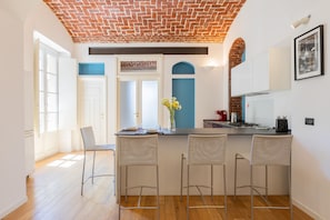 Una cocina con techo de ladrillo, paredes blancas y una barra con dos taburetes.