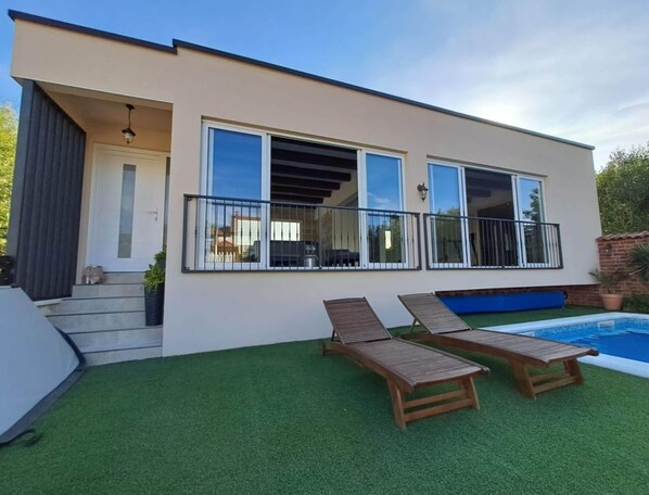 Ein modernes Haus mit Balkon, Schwimmbad und Kunstrasen.