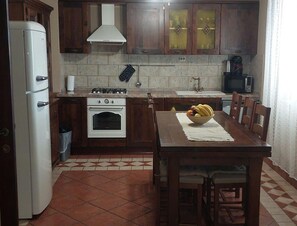 Eine Küche mit Herd, Backofen, Kühlschrank und einem Esstisch mit Stühlen.