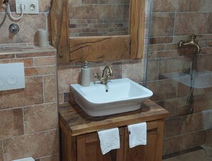Ein Badezimmer mit einem weißen Waschbecken, einem hölzernen Waschtisch und einer Duschkabine aus Glas.