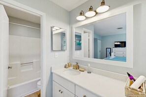 Une salle de bain avec une baignoire, un lavabo, un miroir et un téléviseur en arrière-plan.