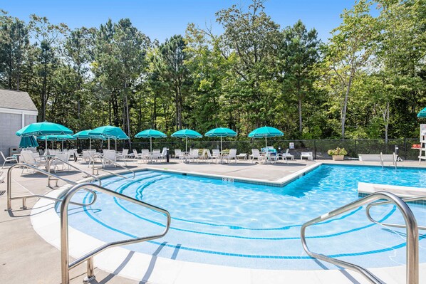 Une piscine entourée d’arbres, avec des chaises longues et des parasols.
