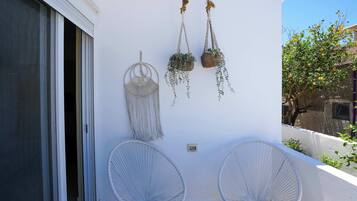 A balcony with two white wire chairs, a macrame wall hanging, and hanging planters.