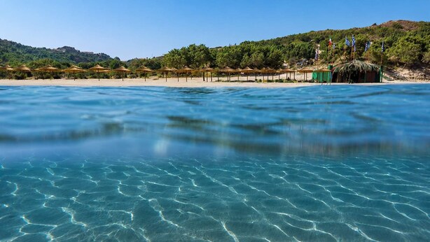 A beach with clear water, umbrellas, and flags on a hillside. - Ambela House, Traditional Living in Kefalos, Kos (Kos)