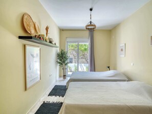 A bedroom with two beds, a ceiling fan, a window with curtains, a plant, and a framed picture on the wall. - Ambela House, Traditional Living in Kefalos, Kos (Kos)