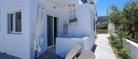 A white building with a balcony, wicker lounge chairs, a small table, and hanging planters.