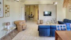 A living room with a sofa, armchair, and a TV mounted on the wall. - Ambela House, Traditional Living in Kefalos, Kos (Kos)