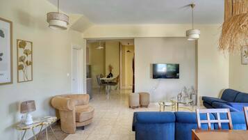 A living room with a sofa, armchair, and a TV mounted on the wall.