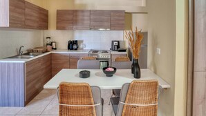 A modern kitchen with wooden cabinets, a white countertop, a dining table with chairs, and a hanging light fixture. - Ambela House, Traditional Living in Kefalos, Kos (Kos)