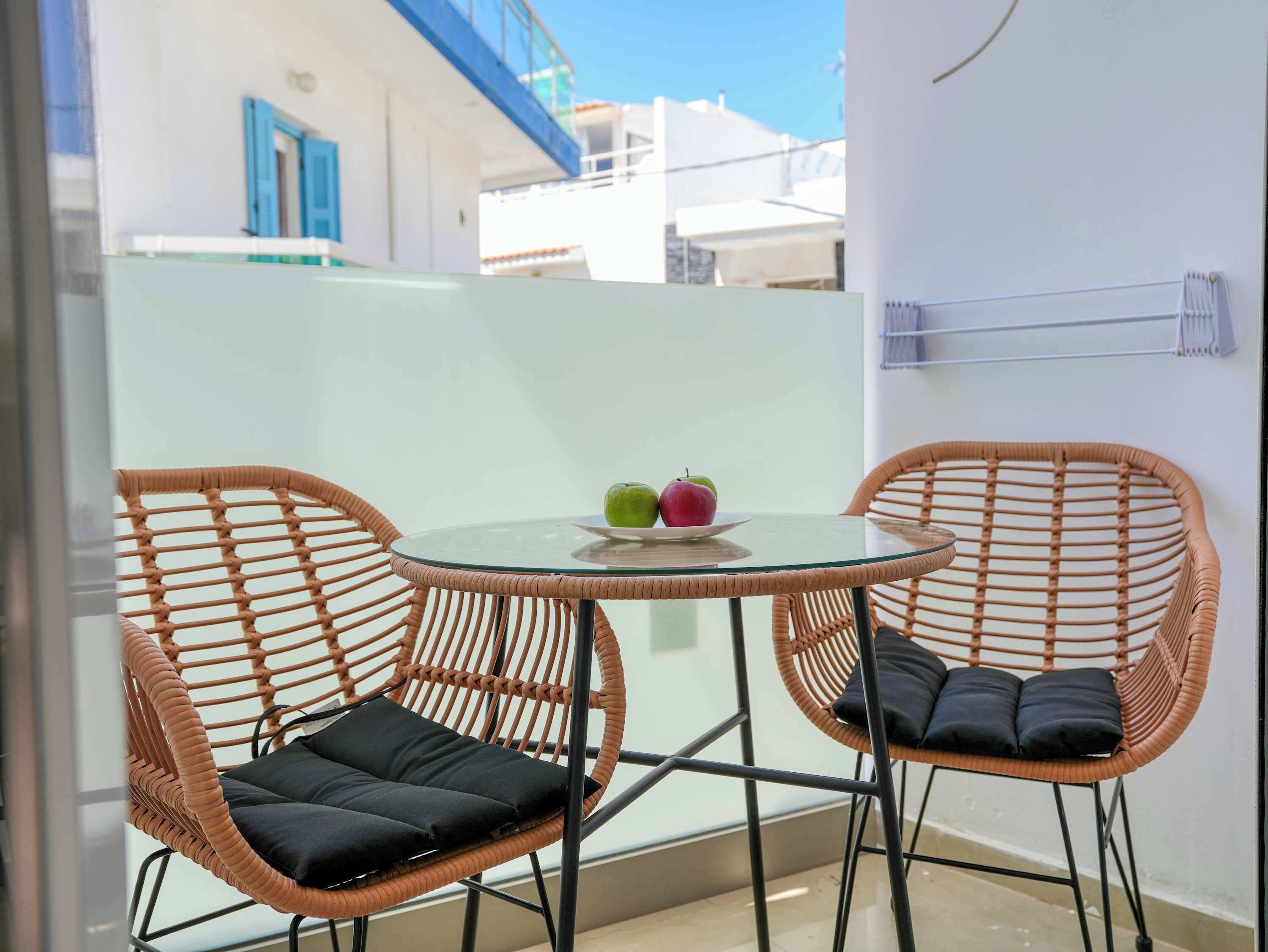 A balcony with two wicker chairs, a glass table, and a plate with apples.